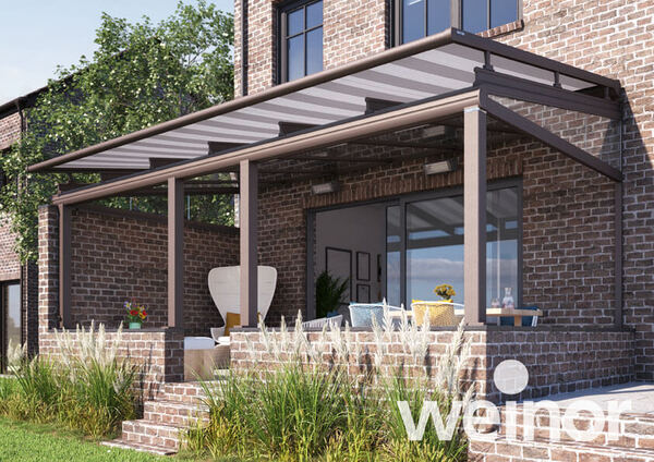 Moderne Terrassenüberdachung aus Glas an Backstein-Haus mit Gartenmöbeln auf Terrasse.