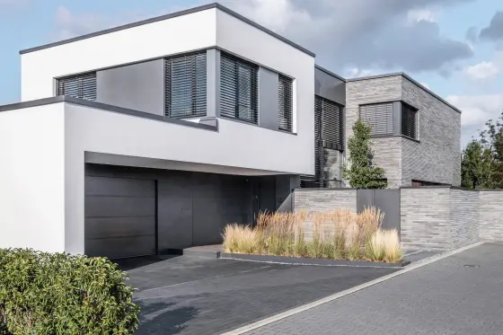 Modernes Einfamilienhaus mit Flachdach, großen Fenstern und gepflegtem Vorgarten.